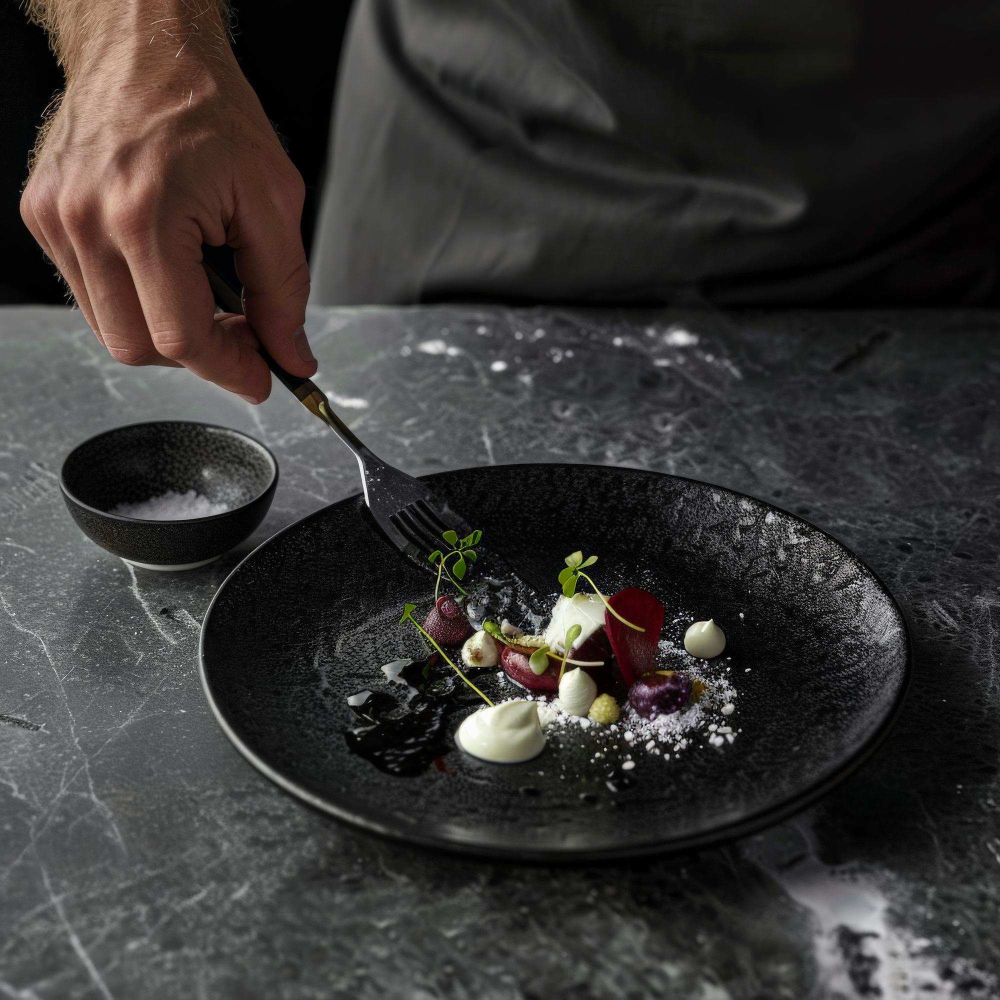 Chef plating an elegant dish on black slate
